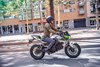 Side angle of a person riding a green electric motorcycle on a street.