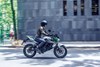 Side angle of a person riding a green electric motorcycle on a road.