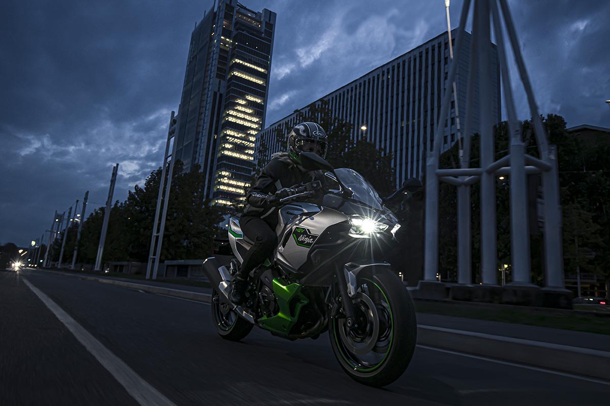 Three-quarter front angle of a person riding a motorcycle in a city at night.
