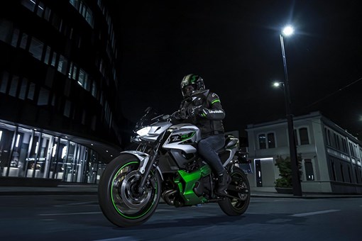 Three-quarter front angle of a person riding a motorcycle on a city street at night. opens in a new window