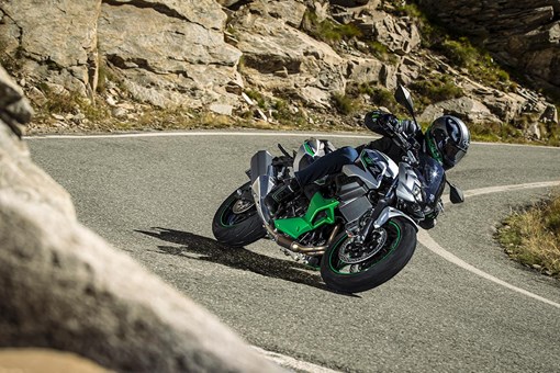 Three-quarter front angle of a person riding a motorcycle around a bend in a road. opens in a new window