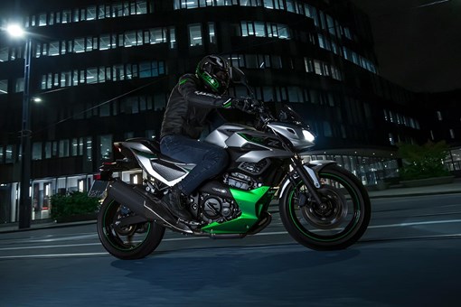 Side angle of a person riding a motorcycle in a city at night. opens in a new window