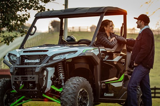 Three-quarter front angle of a parked side x side with two people next to it. opens in a new window