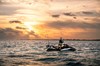 Side angle of a person standing on a personal watercraft at sunset.