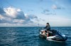 Three-quarter front angle of a person fishing on a personal watercraft in the ocean.