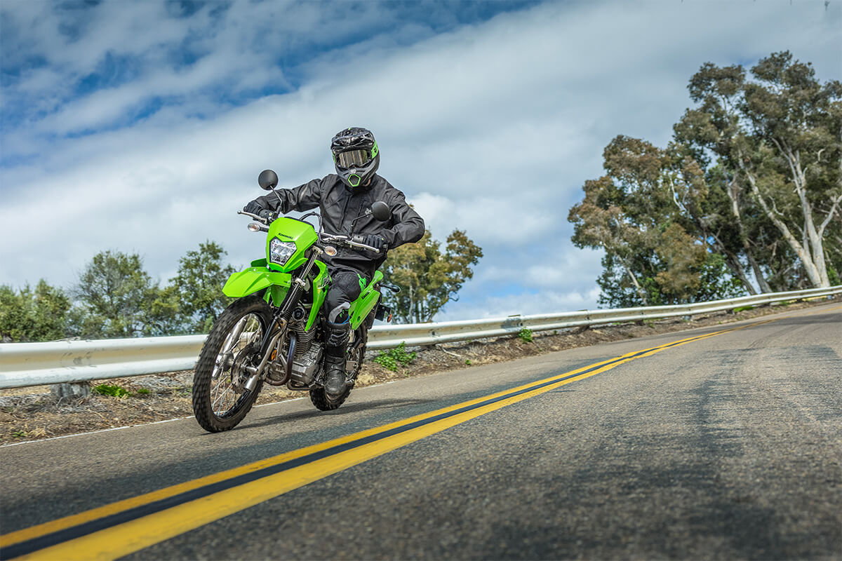 Three-quarter front angle of a person riding a green motorcycle on a highway.