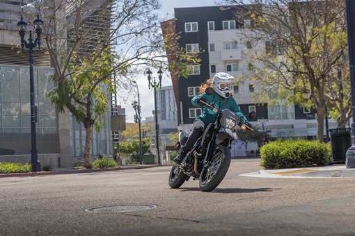 Three-quarter front angle of a person coming out of a turn on a motorcycle in an urban city. opens in a new window
