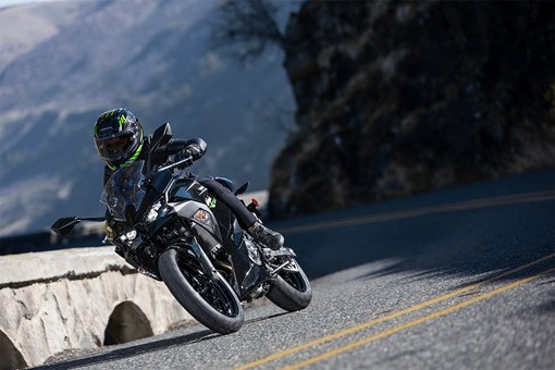 Three-quarter front angle of a person riding a black motorcycle around a bend. opens in a new window