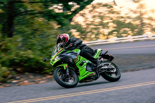 Side angle of a person riding a green motorcycle on a road. opens in a new window