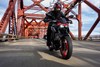 Front angle of a person riding a motorcycle on a bridge.