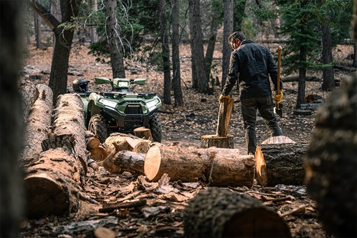 Three-quarter front angle of an ATV parked near a person chopping wood. opens in a new window