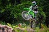 Three-quarter front angle of person riding a motorcycle over a log on a trail.