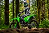 Profile angle of a person seated on a motorcycle on a wooded trail.