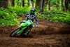 Front angle of a person riding a motorcycle around a corner on a wooded trail.