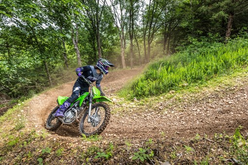 Three-quarter front angle of a person leaning into a turn on a motorcycle off-road.  opens in a new window