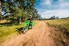 Three-quarter front angle of a person riding a green motorcycle on a dirt trail.