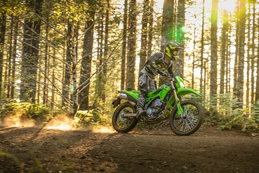 Three-quarter front angle of a person riding a motorcycle through the woods. opens in a new window