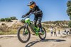 Three-quarter front angle of a young adult riding an electric balance bike on dirt.