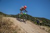 Side angle of a young adult riding an electric balance bike down a dirt hill. 