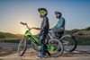 Side angle of two young adults sitting on electric balance bikes parked. 