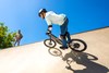 Three-quarter rear angle of a young adult riding an electric balance bike up the outer edge of the skate park.