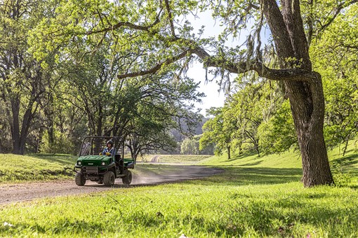Three-quarter front angle of a person driving a side x side on a dirt trail. opens in a new window