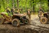 A group of people talking between two side x sides parked off-road in the forest.