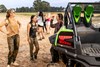 A group of people talking next to a side x side parked off-road.