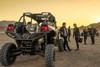 A group of people standing and talking in between two side x sides parked off-road.