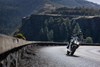 Front angle of a person riding a motorcycle on a highway with trees in the background.