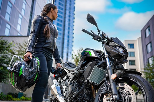 Three-quarter front angle of a person standing next to a motorcycle. opens in a new window