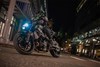 Three-quarter front angle of a person riding a motorcycle on a city street at night.