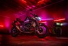 Side angle of a motorcycle staged in a warehouse with neon lights.