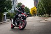 Three-quarter front angle of a person riding a motorcycle on a city street.