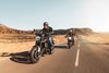 Three-quarter front angle of two people riding motorcycles on highway.