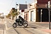 Side angle of a person riding a motorcycle across an intersection.