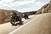 Three-quarter front angle of two people riding motorcycles on a highway.