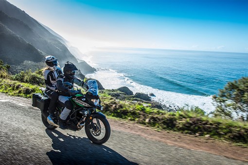 Three-quarter front angle of a person and a passenger riding a motorcycle on a scenic highway. opens in a new window