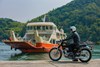 Side angle of a person seated on a motorcycle in front of a boat.