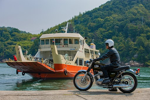 Side angle of a person seated on a motorcycle in front of a ferry boat. opens in a new window