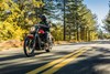 Three-quarter front angle of a person riding a motorcycle on a highway with trees in the background.