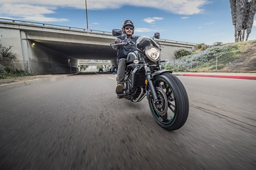 Three-quarter front angle of a person riding a motorcycle on a street near the freeway. opens in a new window