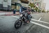 Three-quarter front angle of a person riding a motorcycle on a city street.