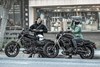 Side angle of two people getting ready to ride their motorcycles through the city.