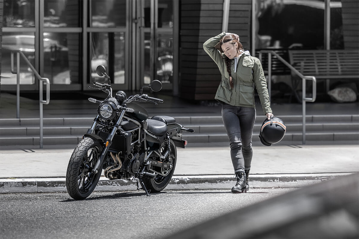 Three-quarter front angle of a person standing next to a motorcycle in front of a building.