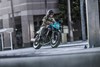 Three-quarter front angle of a person riding a motorcycle on a city street.