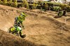 Three-quarter front angle of a kid riding an electric balance bike on a dirt track with an adult supervising.