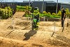 Three-quarter front angle of a kid riding an electric balance bike on a dirt track with a parent in the background.