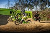 Three-quarter front angle of two kids riding a electric balance bikes on a dirt track with a parent watching.