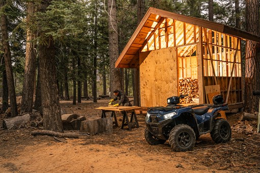 Front three-quarter view of an ATV parked in front of a cabin. opens in a new window